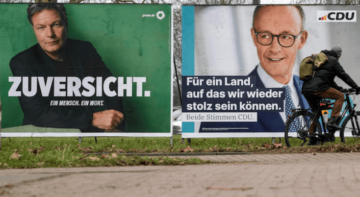 Wahlplakate von Robert Habeck und Friedrich Merz für die Bundestagswahl an einer Straße – ein Radfahrer fährt vorbei.