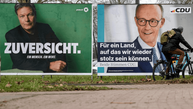 Wahlplakate von Robert Habeck und Friedrich Merz für die Bundestagswahl an einer Straße – ein Radfahrer fährt vorbei.