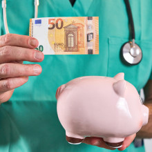 Eine Person im Arztkittel schmeißt 50 Euro in ein Sparschwein.