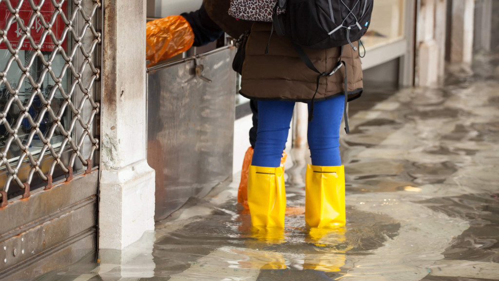 Mädchen steht bei Hochwasser in Gummistiefeln auf einem Platz in Venedig