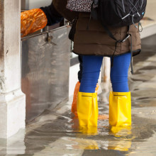 Mädchen steht bei Hochwasser in Gummistiefeln auf einem Platz in Venedig