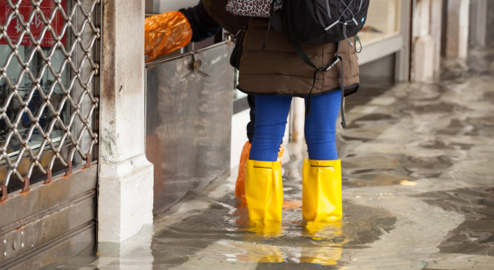 Mädchen steht bei Hochwasser in Gummistiefeln auf einem Platz in Venedig