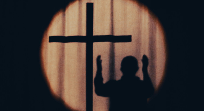 Schattenriss eines Mannes mit erhobenen Händen neben einem Kreuz