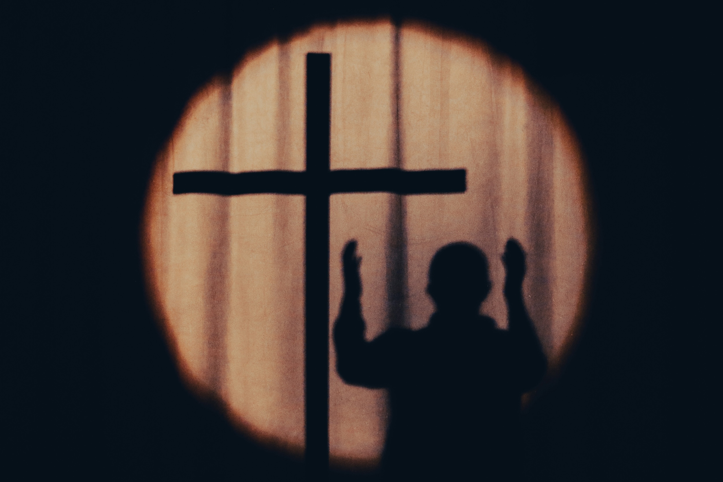 Schattenriss eines Mannes mit erhobenen Händen neben einem Kreuz