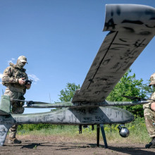 Ein Soldat steht mit einer Fernbedienung neben einer Drohne, ein anderer kniet davor