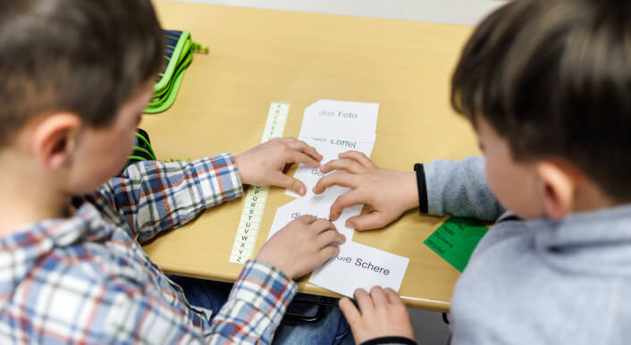 Zwei Jungen sitzen in einer Grundschule an einem Tisch und üben zu lesen.