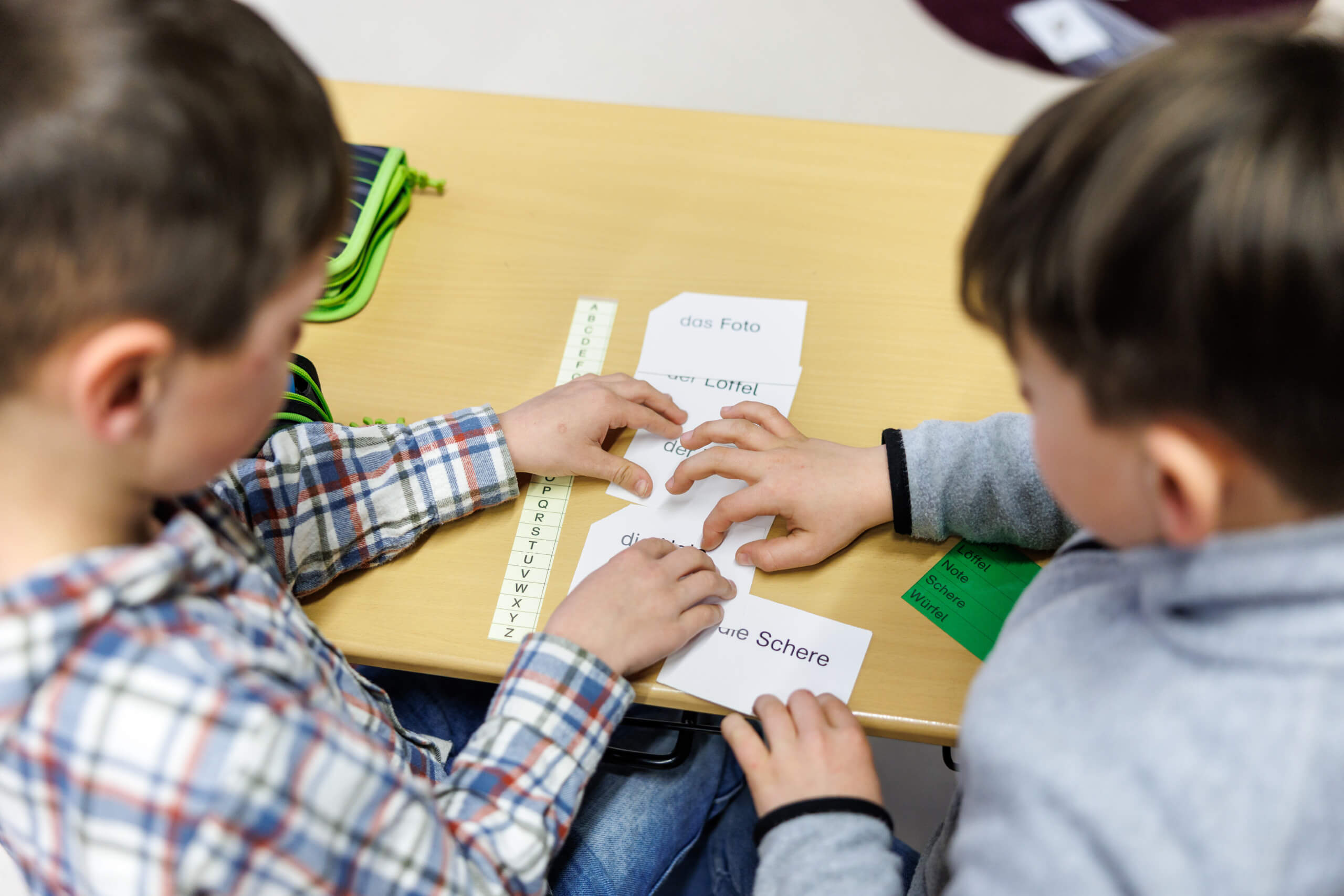 Zwei Jungen sitzen in einer Grundschule an einem Tisch und üben zu lesen.