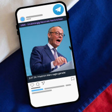 Ein Smartphone, auf dem ein Telegram-Beitrag zu sehen ist liegt auf einer russischen Flagge