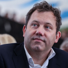 Lars Klingbeil sitzt bei der Cranger Kirmes zwischen Menschen. Er trägt ein dunkles Sakko und ein weißes Hemd.
