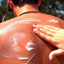 Hand verteilt Sonnencreme auf dem Rücken eines Mannes