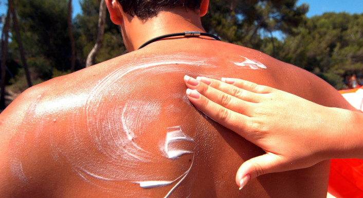 Hand verteilt Sonnencreme auf dem Rücken eines Mannes