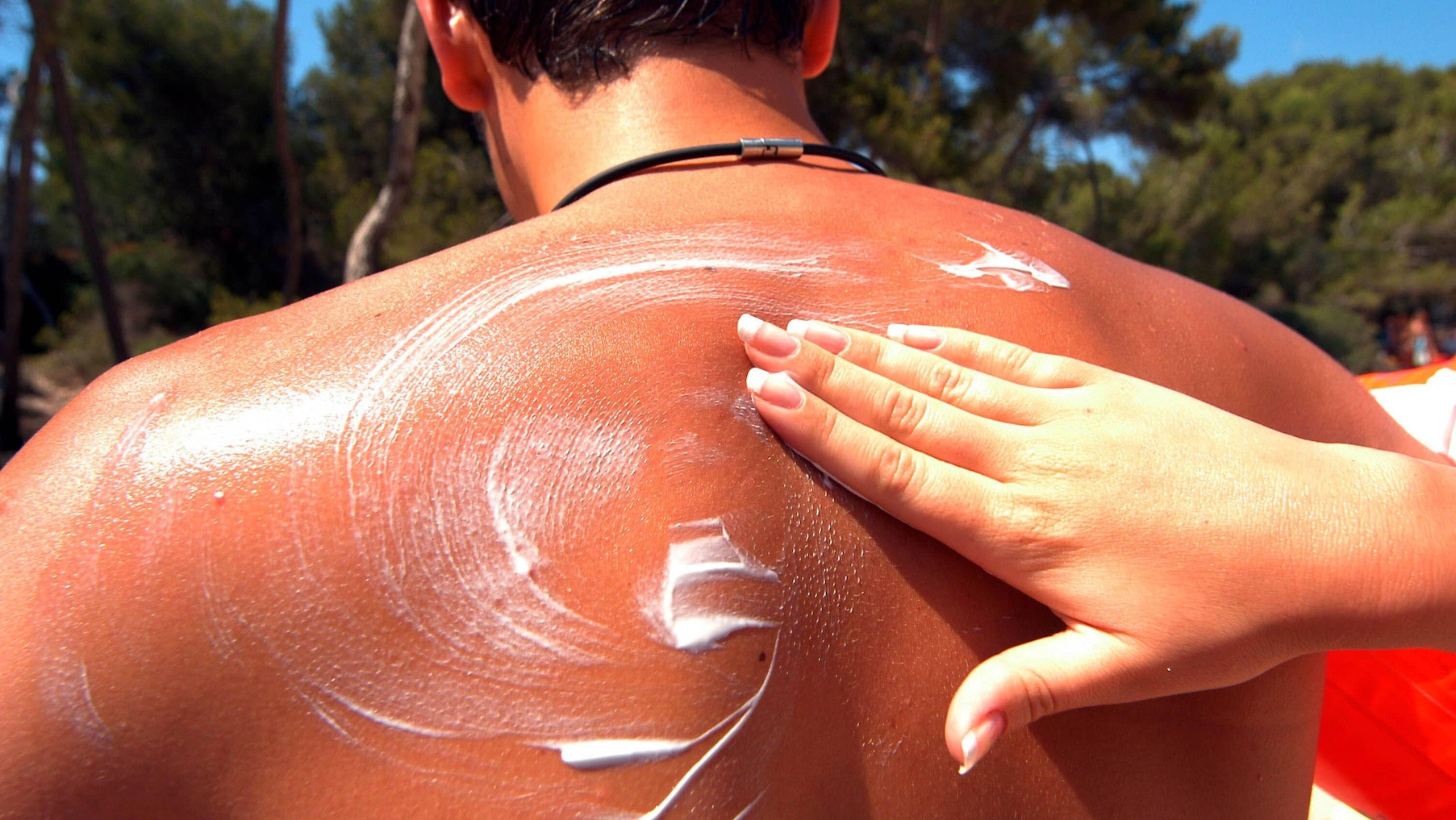 Hand verteilt Sonnencreme auf dem Rücken eines Mannes
