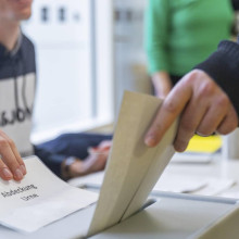 Person wirft einen Wahlzettel in die Wahlurne, Symbolbild zur Landtagswahl in Nordrhein-Westfalen (NRW)