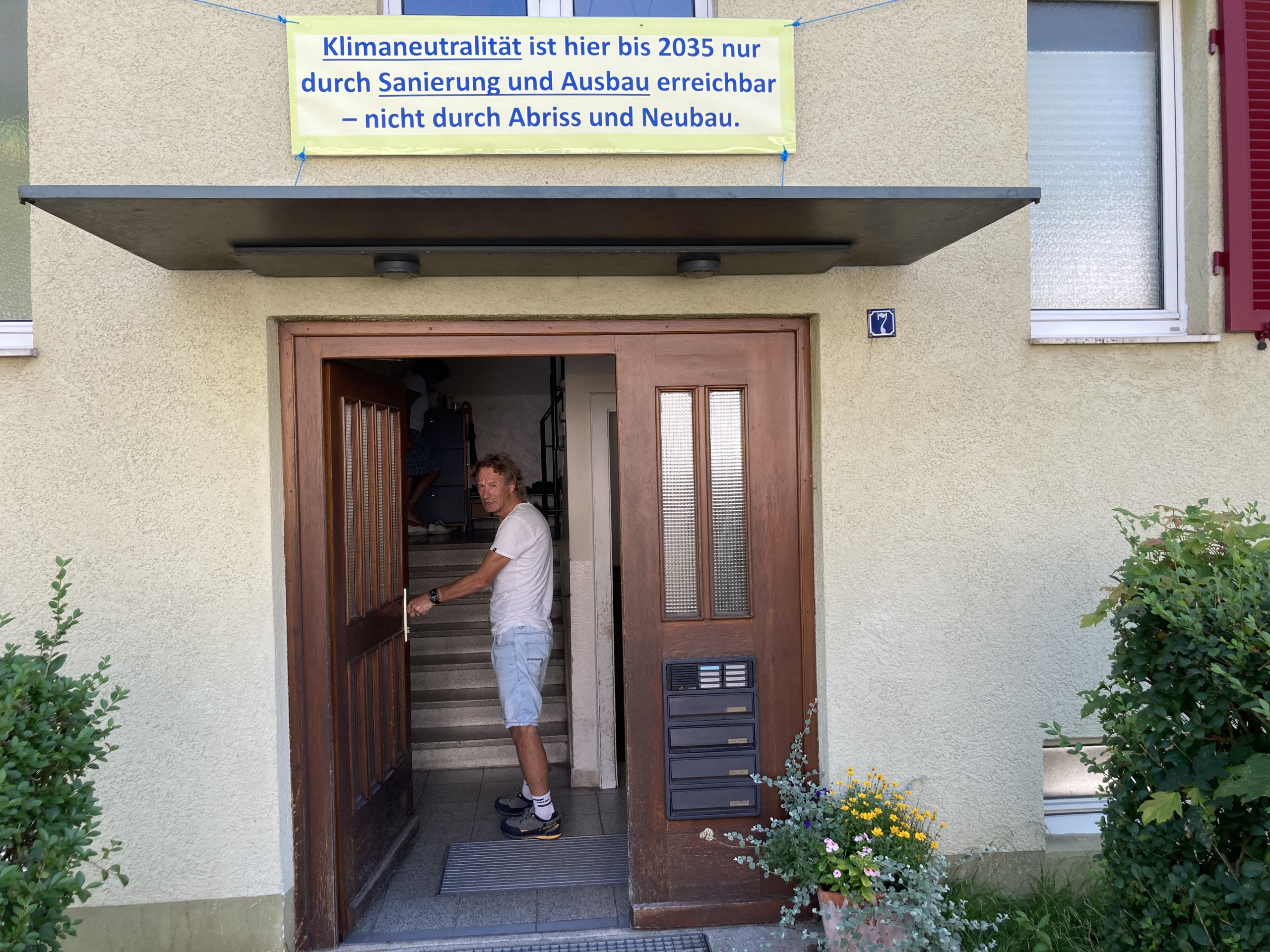 Urs Egger öffnet die Haustür in der August-Ganther-Straße 7, darüber ein Protestbanner. Credits: Marius Münstermann