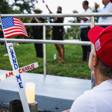 Frau hockt mit Trump-Cappy vor einem Kreuz
