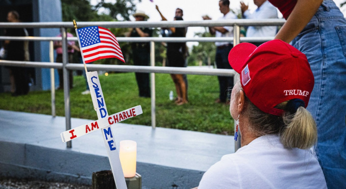 Frau hockt mit Trump-Cappy vor einem Kreuz