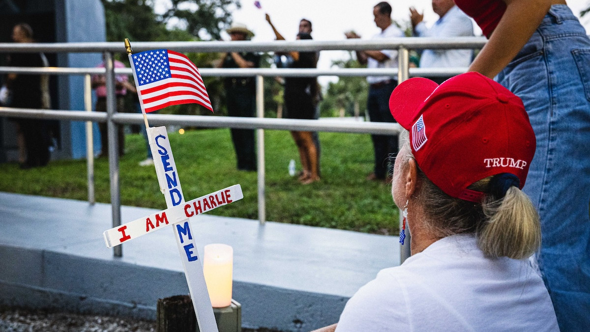 Frau hockt mit Trump-Cappy vor einem Kreuz