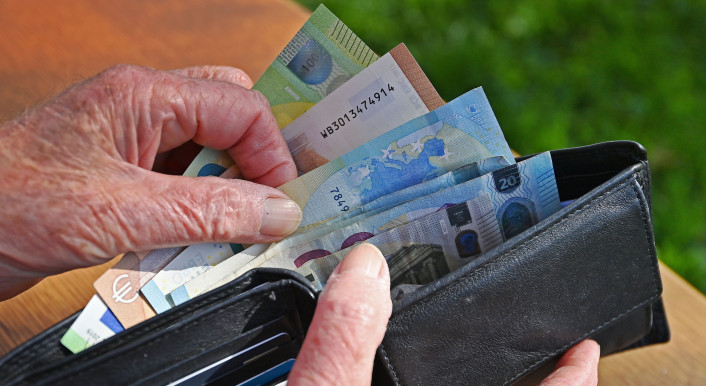 Eine ältere Person öffnet ein Lederportemonnaie und zieht mehrere Euro-Scheine daraus hervor