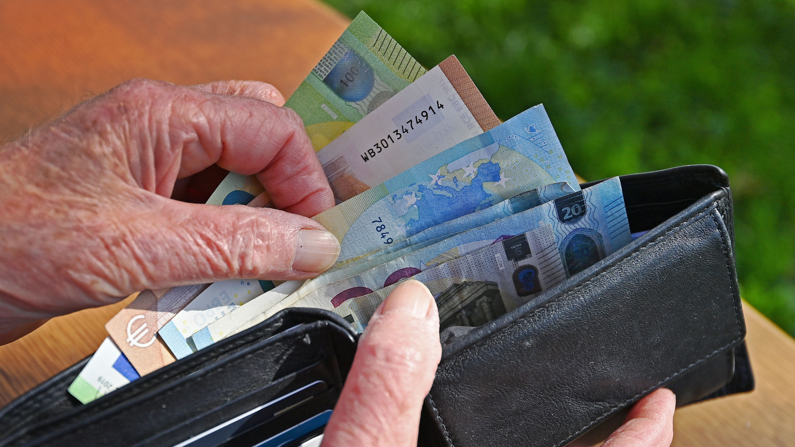 Eine ältere Person öffnet ein Lederportemonnaie und zieht mehrere Euro-Scheine daraus hervor