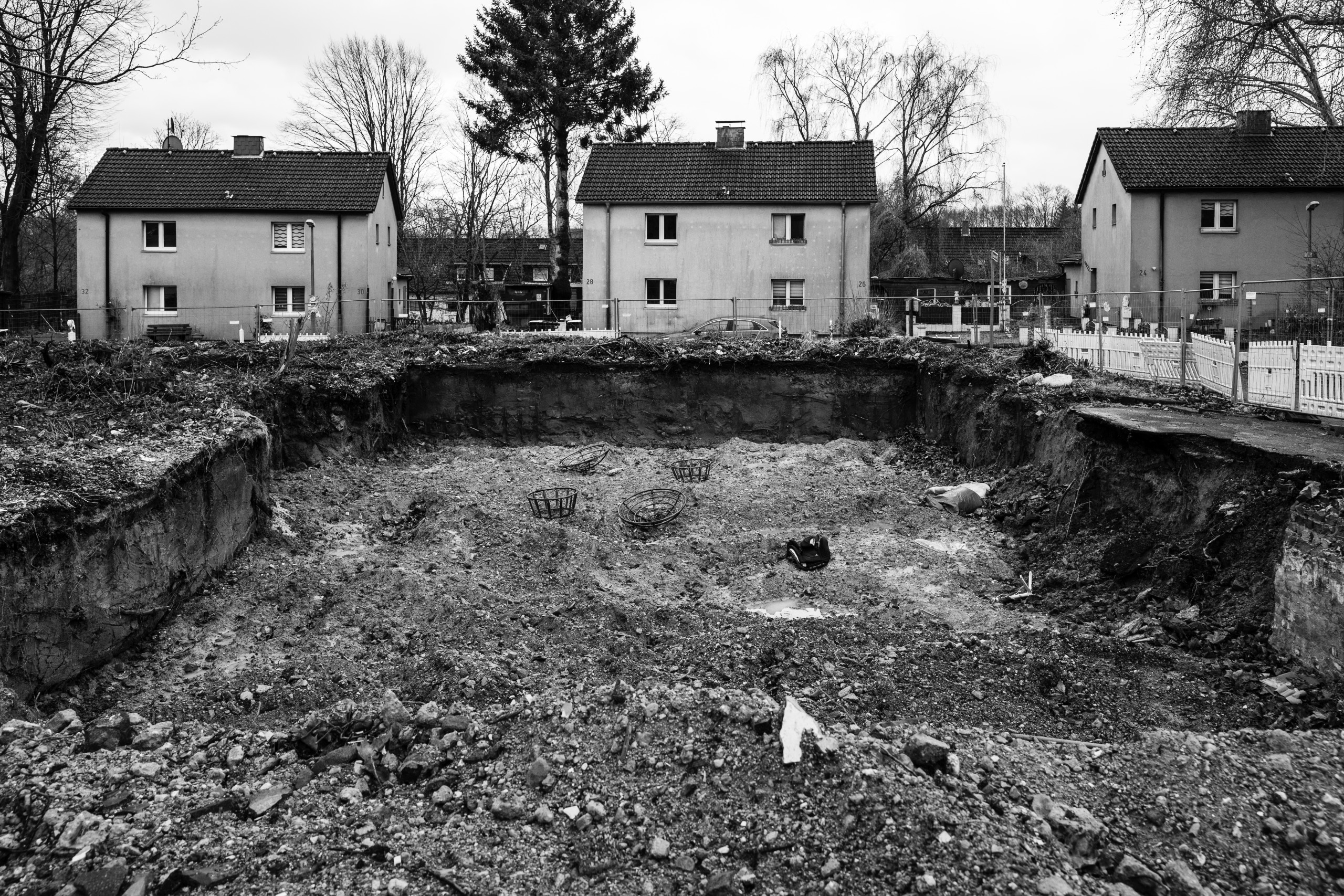 Ein Loch, gefüllt mit Bauschutt, umgeben von Bauzäunen. Im Hintergrund stehen Wohnhäuser.