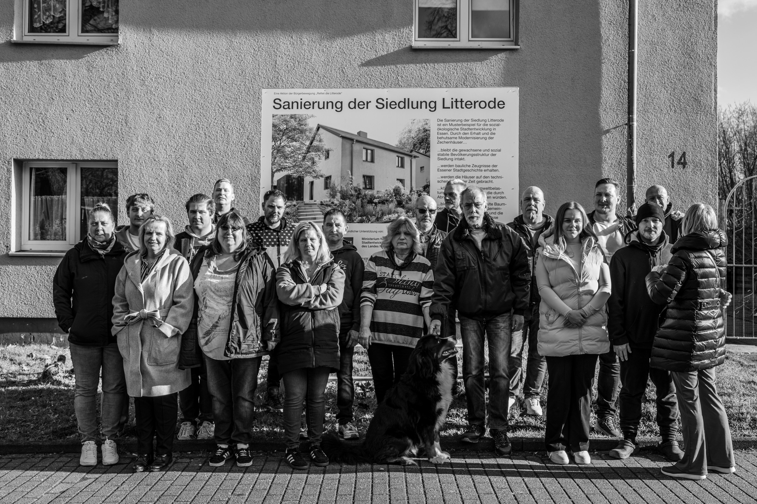 Eine Gruppe von Menschen vor einem Schild. Darauf steht: "Sanierung der Siedlung Litterode"