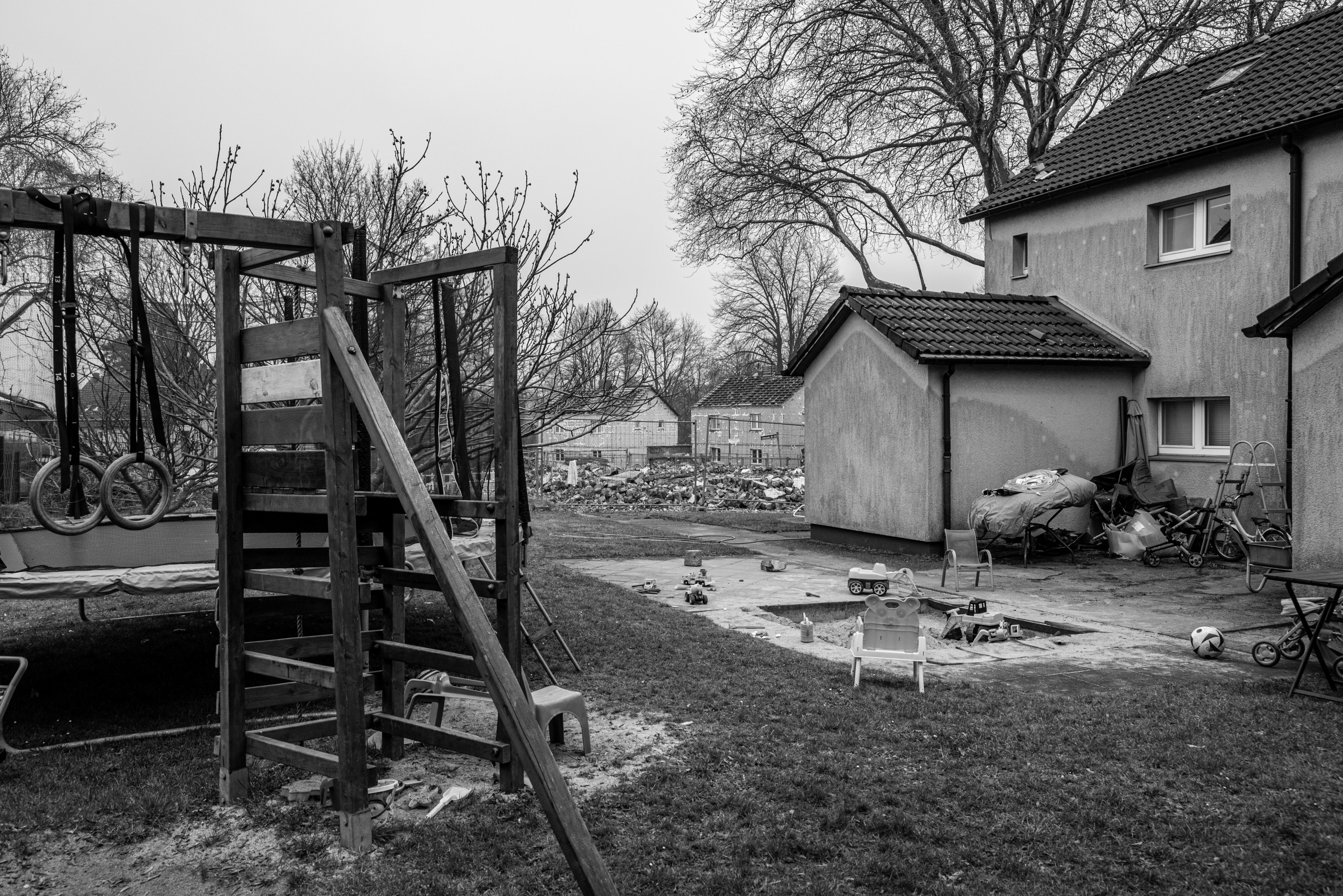 Ein Garten mit Klettergerüst und Kinderspielzeug, im Hintergrund ein Bauzaun, dahinter der Bauschutt abgerissener Häuser