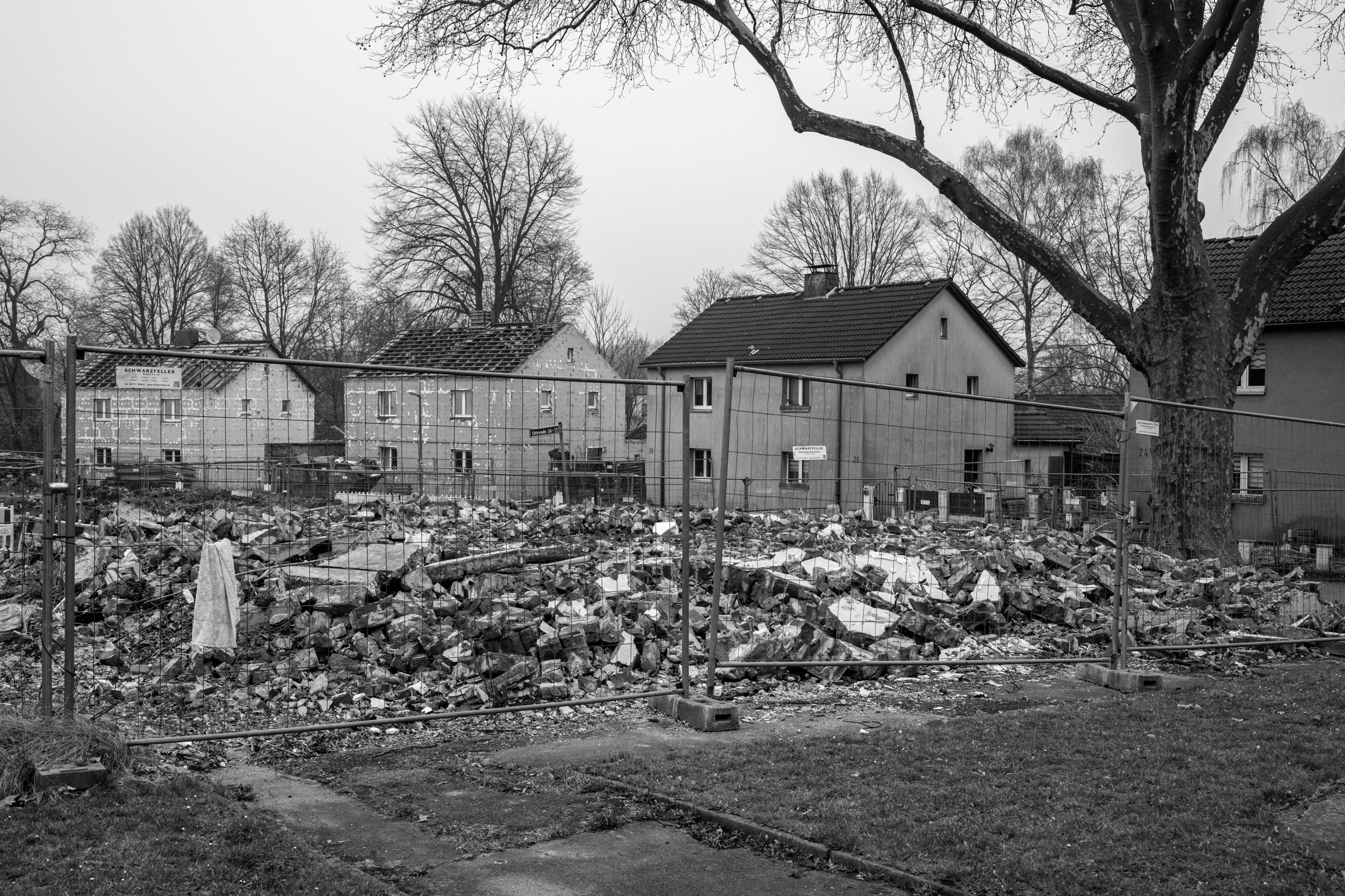 Ein Haufen Bauschutt von abgerissenen Wohnhäusern hinter einem Bauzaun. Im Hintergrund stehen weitere Wohnhäuser.