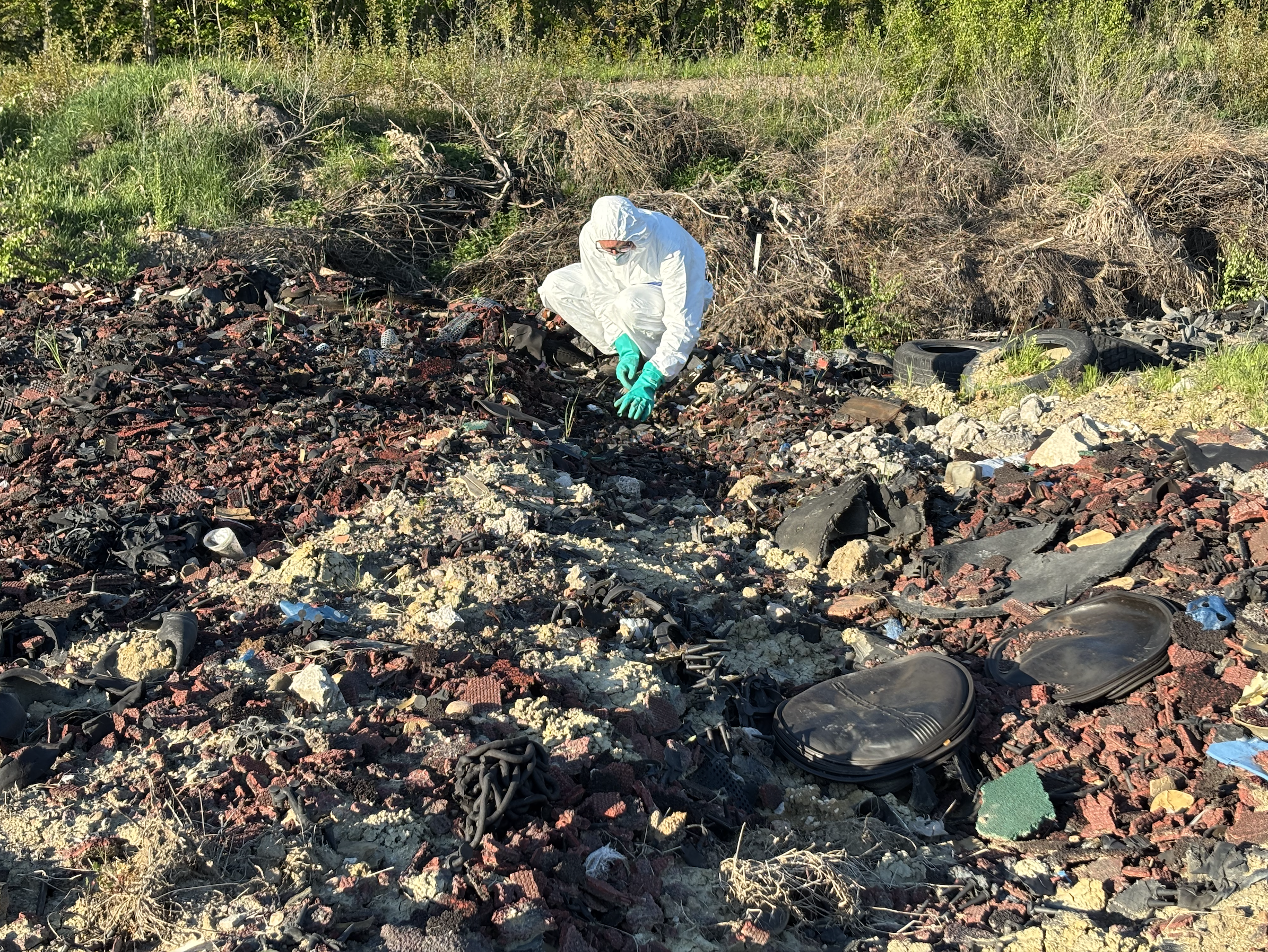 Ein Mensch in weißem Ganzkörperschutzanzug hockt in einem Haufen Müll