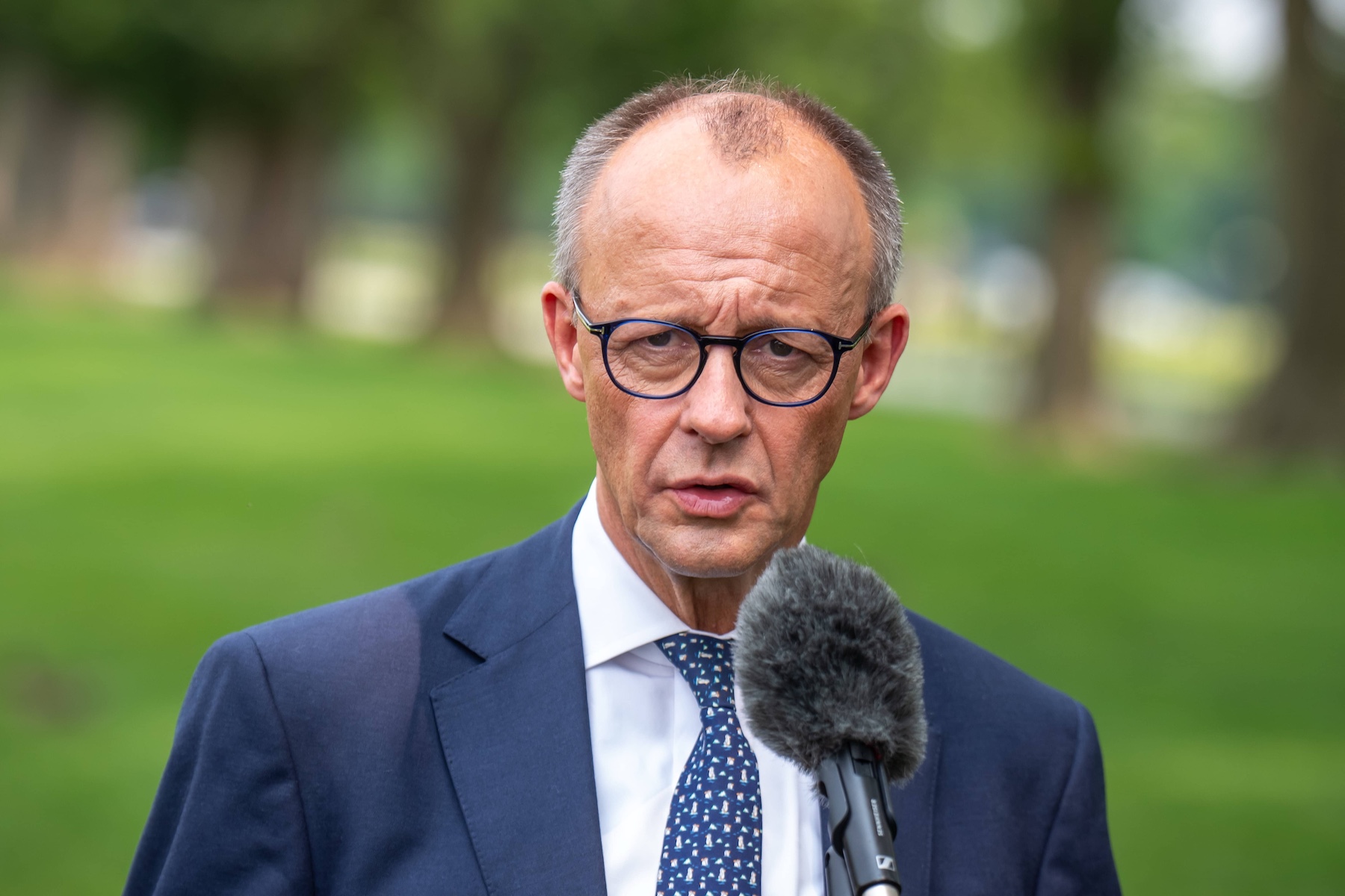 Porträt von Friedrich Merz im Anzug vor einem Mikrofon in einem Park