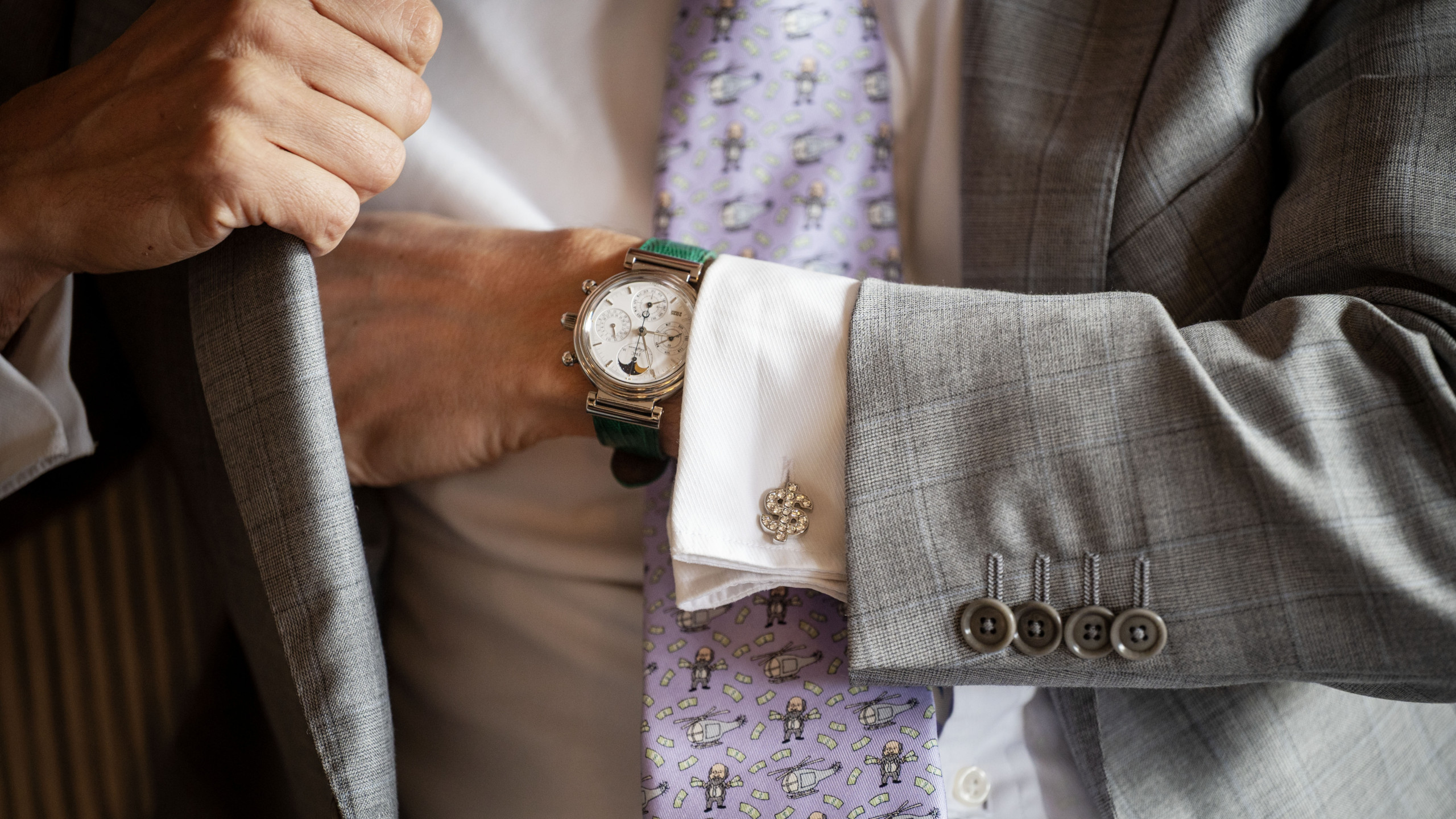 Ein Mann im edlen grauen Anzug greift in seine Innentasche. So als würde er etwas verstecken wollen. An der Hand trägt eine Luxus-Uhr. Ein Dollar-zeichen mit Diamanten ist sein Knopf am Hemd. Er hat auch eine rosa Krawatte. Darauf ist ein Comic-mässig gezeichnetes Muster. Ein Mann mit Bargeld und ein Helikopter.