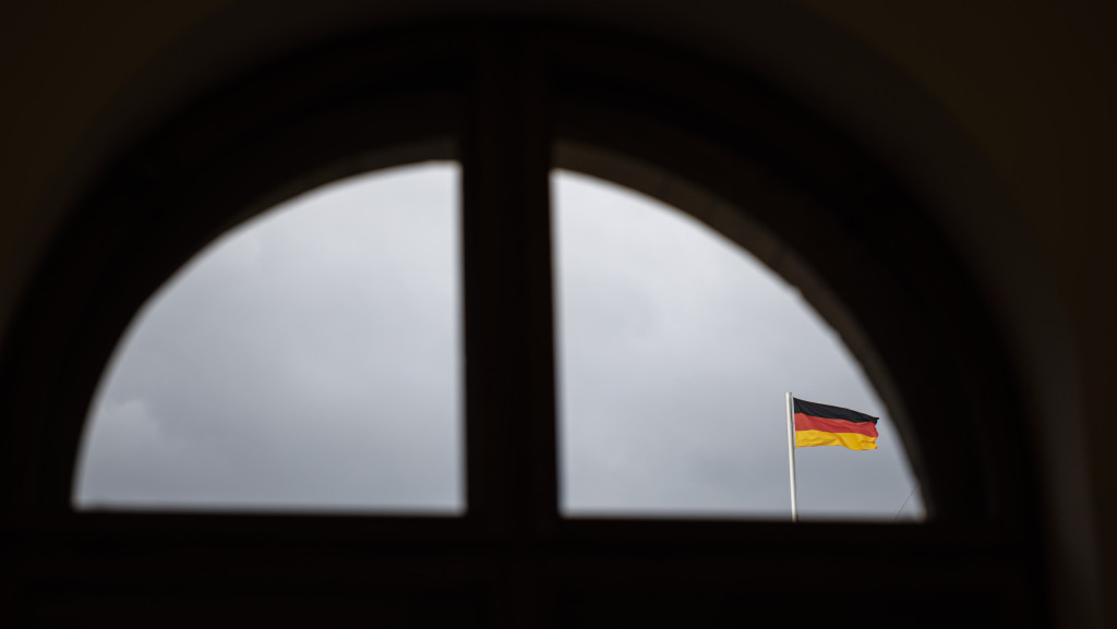 Eine Deutschlandfahne vor grauem Himmel durch ein Fenster fotografiert