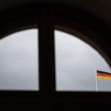 Eine Deutschlandfahne vor grauem Himmel durch ein Fenster fotografiert