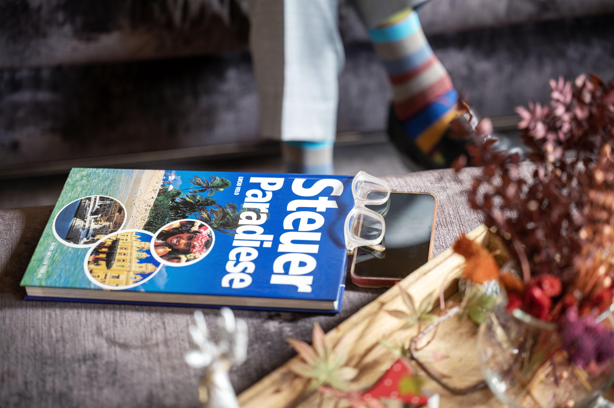 Das Buch „Steuerparadiese“ des Tessiner Anwalts Lucio Velo auf einem Tisch neben einem Smartphone und einer Brille.