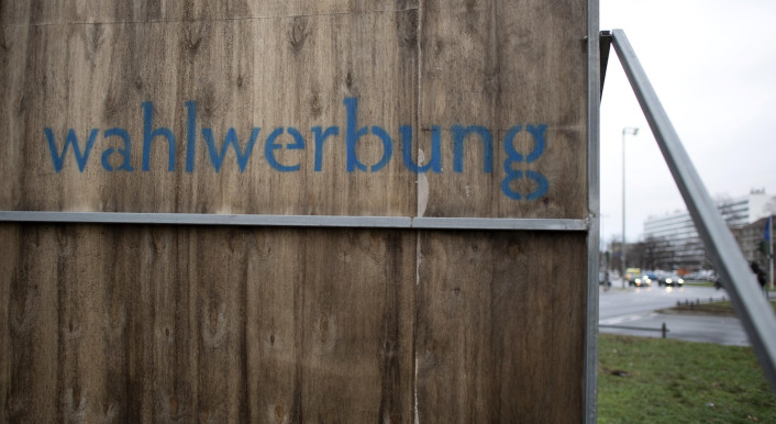 „Wahlwerbung“ steht hinten auf einer Werbetafel an einer Straße