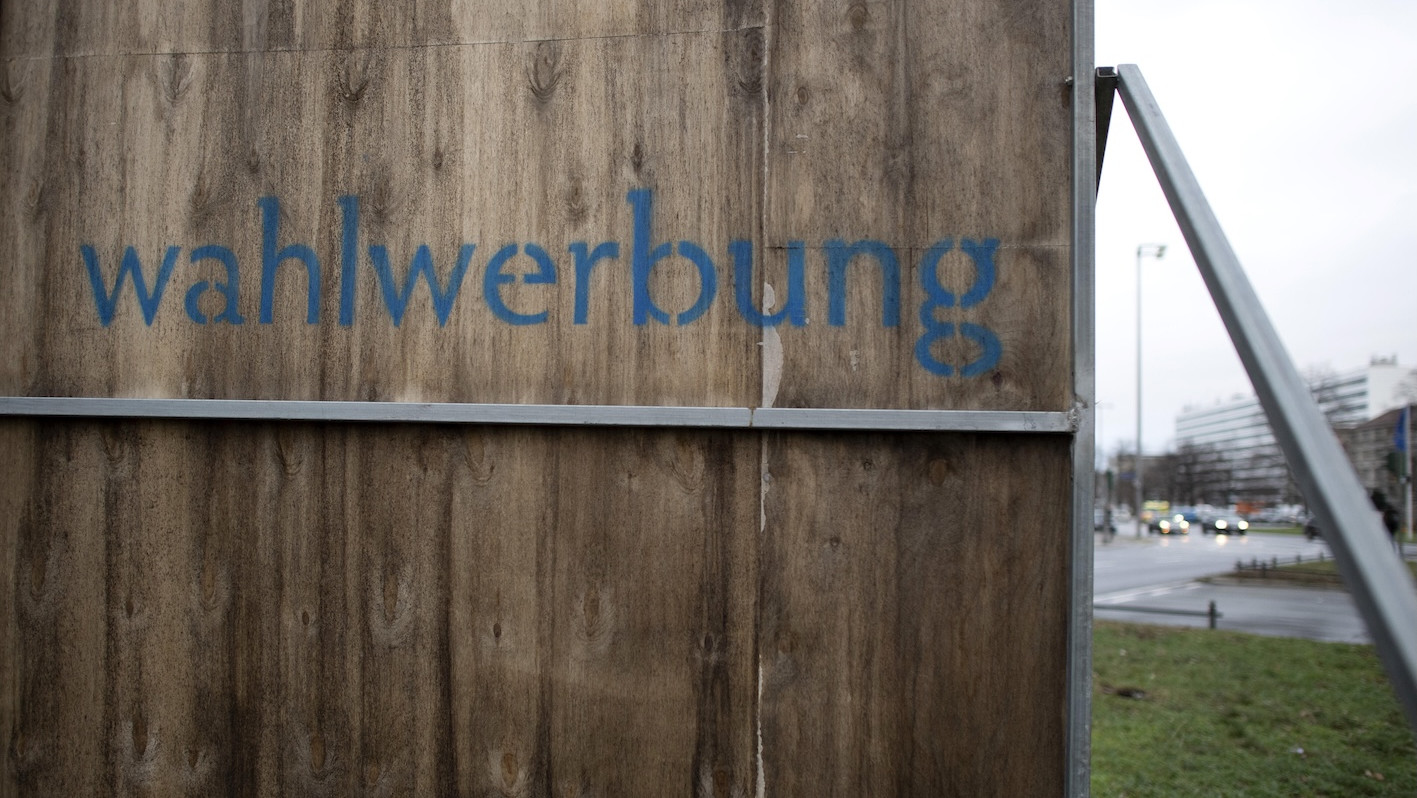 „Wahlwerbung“ steht hinten auf einer Werbetafel an einer Straße