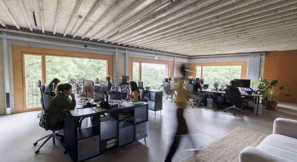 Eine Bürosituation mit zwei Doppeltischreihen und einer Person, die im Vordergrund verschwommen an der Kamera vorbeiläuft