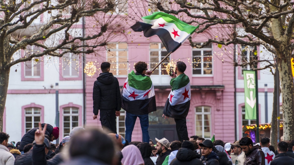 Drei Männer stehen in syrische Fahnen gehüllt auf einer Erhöhung inmitten einer Menschenmenge in Mainz