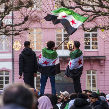 Drei Männer stehen in syrische Fahnen gehüllt auf einer Erhöhung inmitten einer Menschenmenge in Mainz