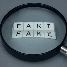 Eine Lupe zeigt auf die Wörter "Fakt" und "Fake".