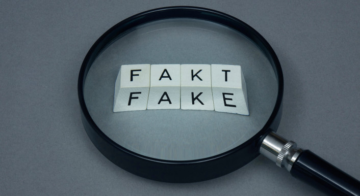 Eine Lupe zeigt auf die Wörter "Fakt" und "Fake".