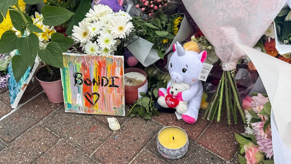 Auf dem Pflastersteinen liegen Blumen und Stofftiere, auf einer Leinwand steht "Bondi".