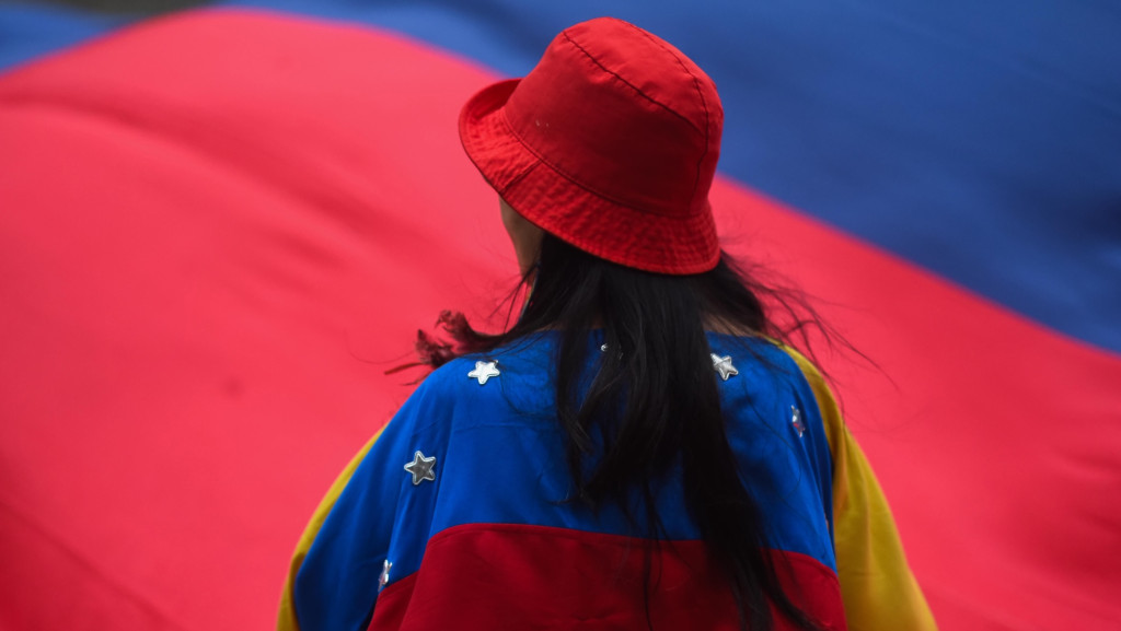Eine Frau mit rotem Hut von hinten mit ungehangener Venezuela-Flagge, im Hintergrund eine weitere große Venezuela-Flagge