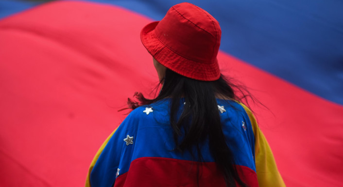Eine Frau mit rotem Hut von hinten mit ungehangener Venezuela-Flagge, im Hintergrund eine weitere große Venezuela-Flagge
