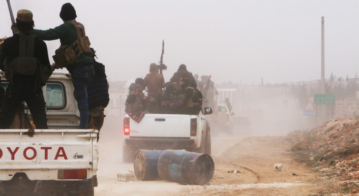 Das Foto zeigt zwei Trucks, die auf einer staubigen Straße in Syrien fahren. Auf den Ladeflächen sind vermummte Kämpfer zu sehen.