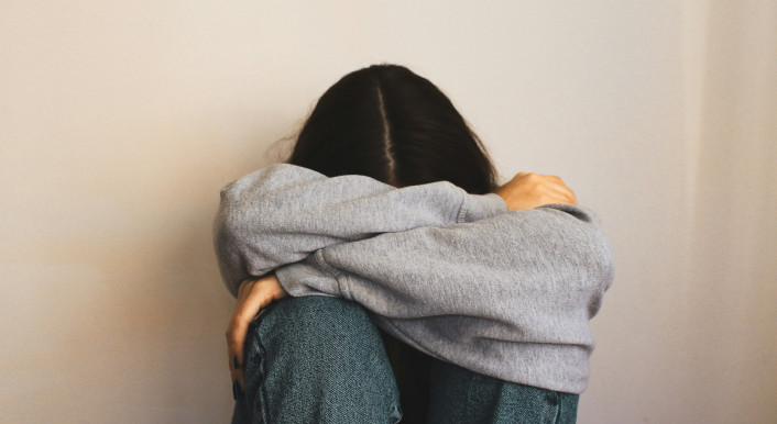 Ein Mädchen sitzt auf dem Boden und verbirgt ihr Gesicht in den Armen.