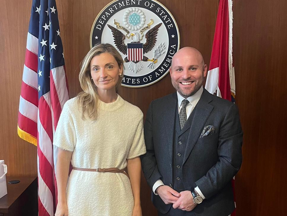 Sarah Rogers und Markus Frohnmaier vor einer US-Flagge und dem Symbol des Department of State.