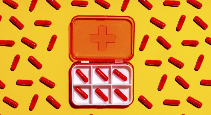 Eine Dose mit roten Kapseln, drumherum weitere rote Kapseln in einem Muster