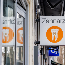 Ein Zahnarzt-Schild an einem Gebäude, gespiegelt in einer Scheibe