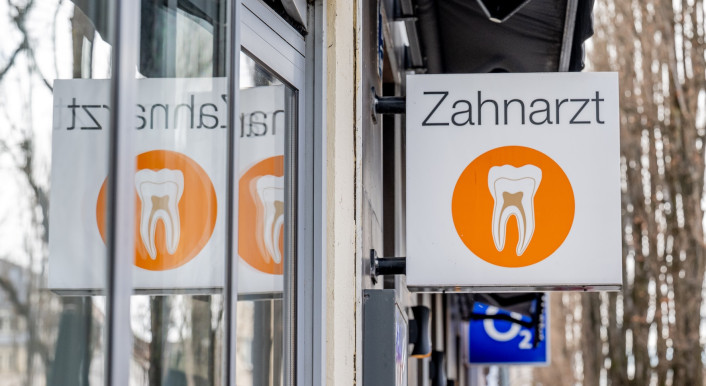 Ein Zahnarzt-Schild an einem Gebäude, gespiegelt in einer Scheibe