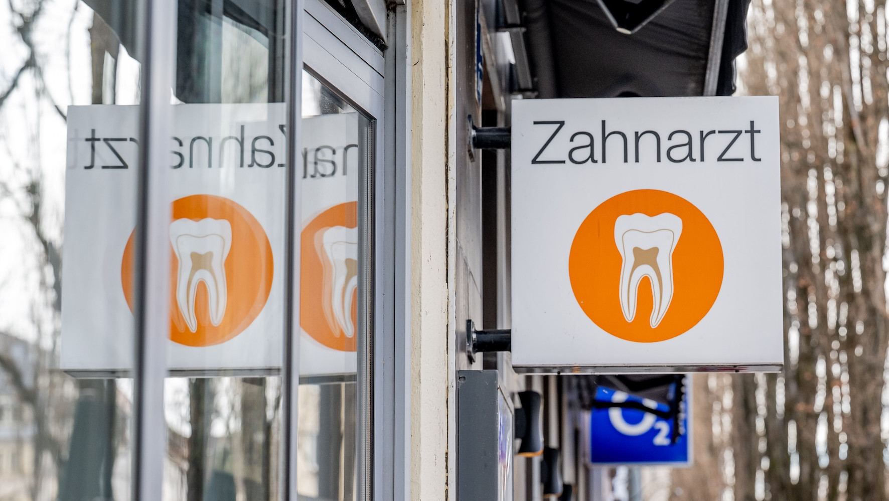Ein Zahnarzt-Schild an einem Gebäude, gespiegelt in einer Scheibe